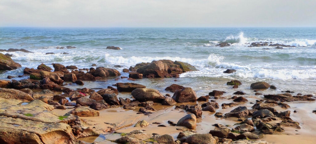 Rocky shoreline with waves breaking on the rocks along a sandy beach.